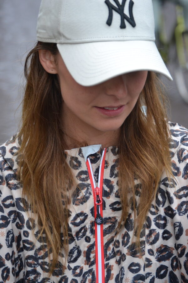 Close-up van een vrouw in een beige leopard regenponcho met rode waterdichte rits en capuchon, ideaal voor regenachtige dagen.