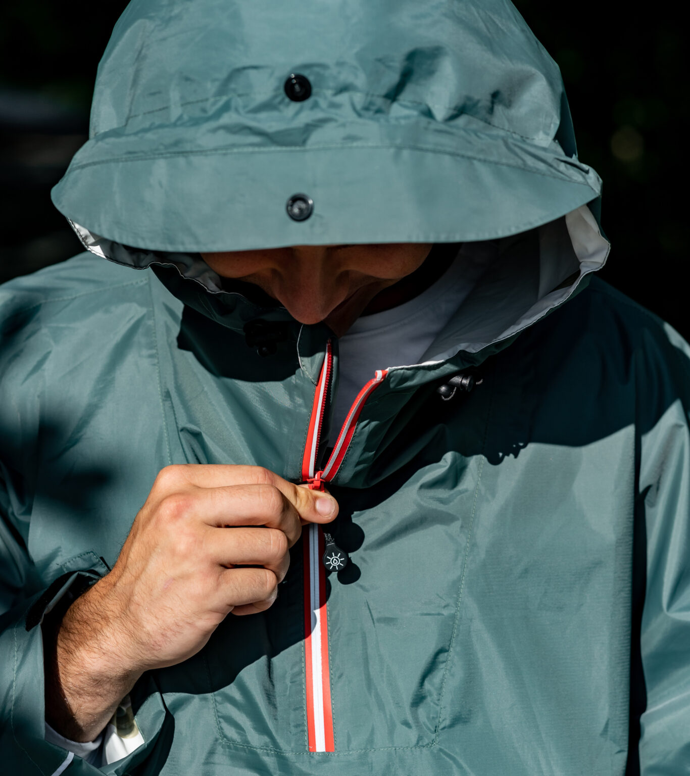 Close-up van een persoon die de waterdichte rits van een groene regenjas met capuchon dichtdoet. Ideaal voor regenachtige dagen en outdoor activiteiten.